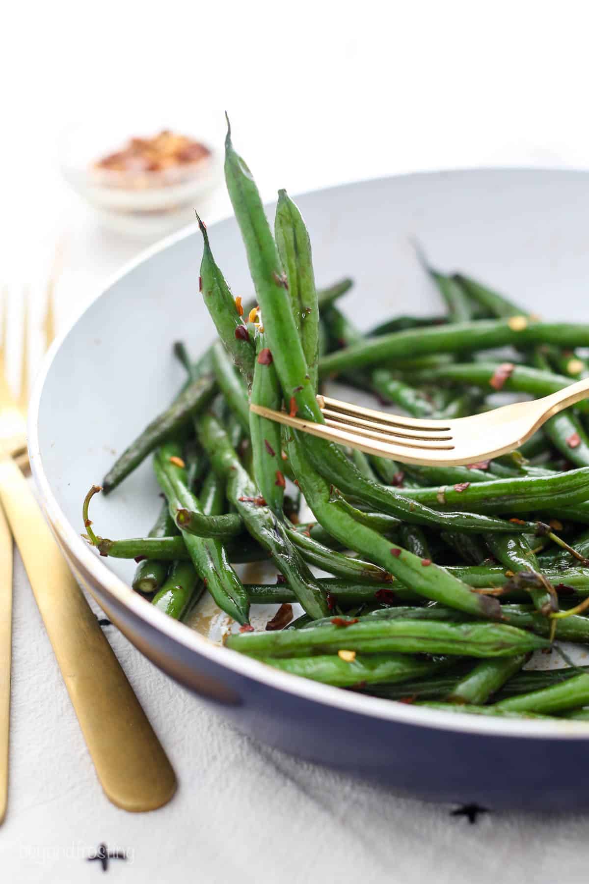 side view of a forkful of cooked green beans held over a plate