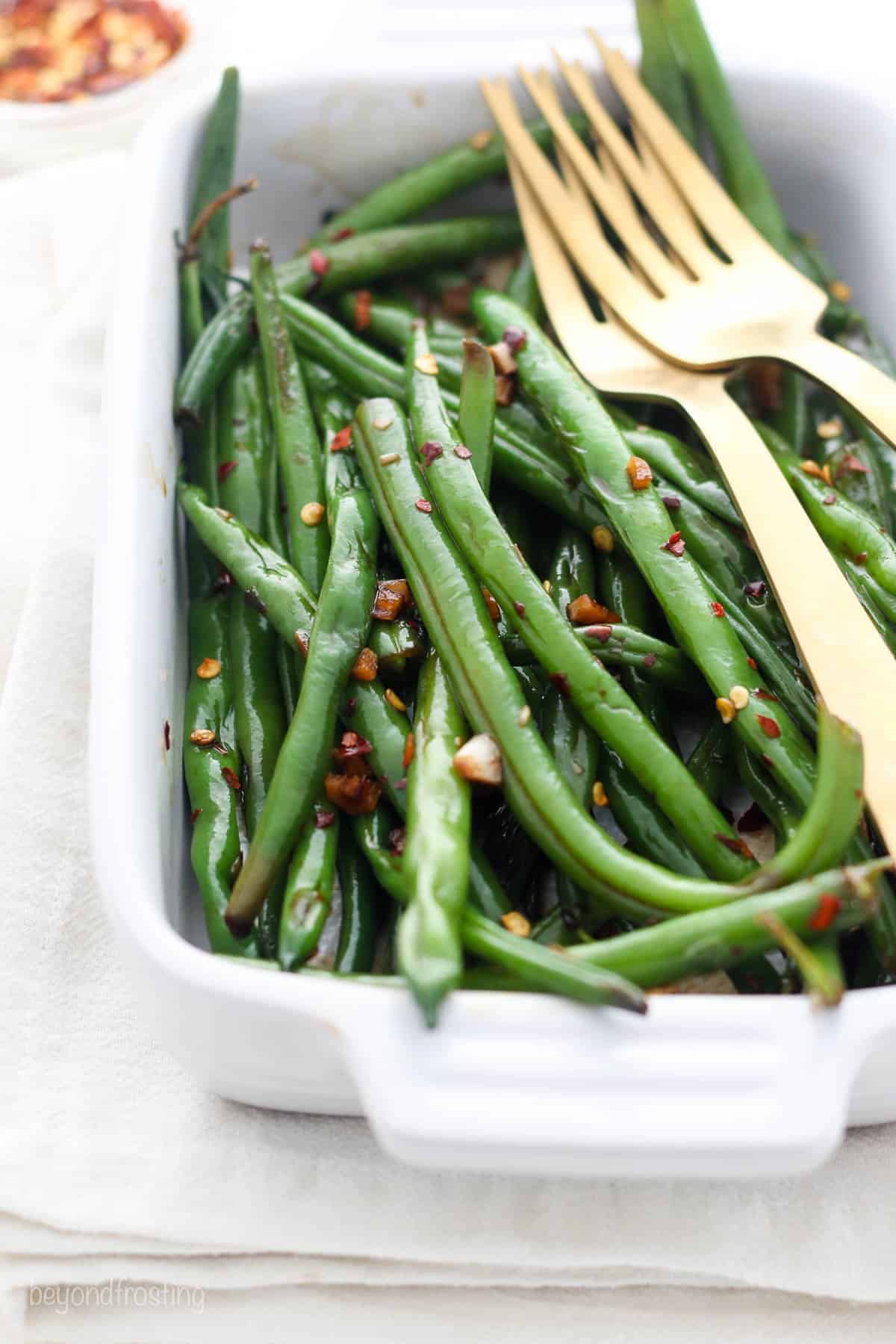 closeup of a dish full of green beans with two forks laying on top