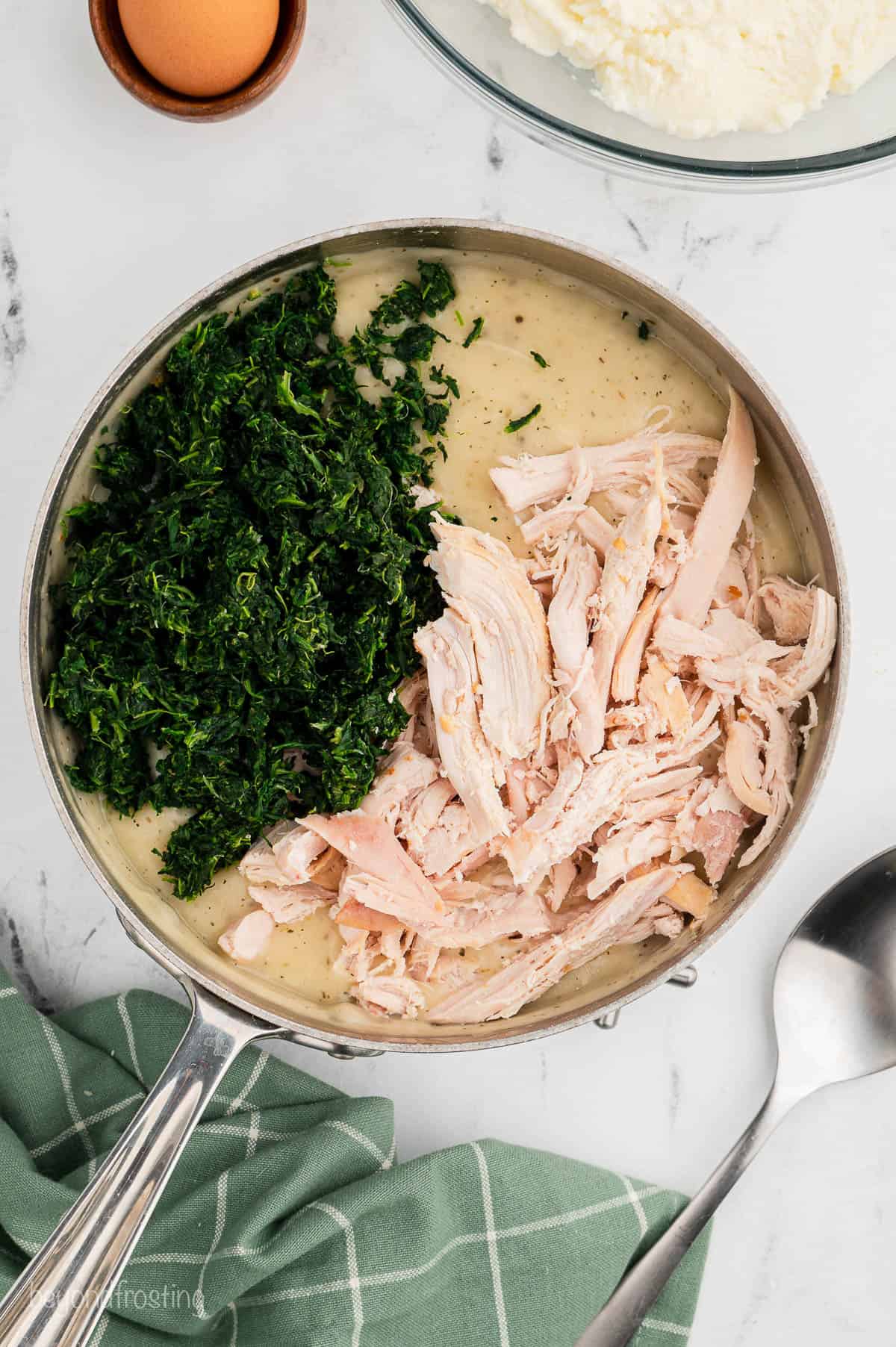 Shredded chicken and spinach added to white sauce in a pan