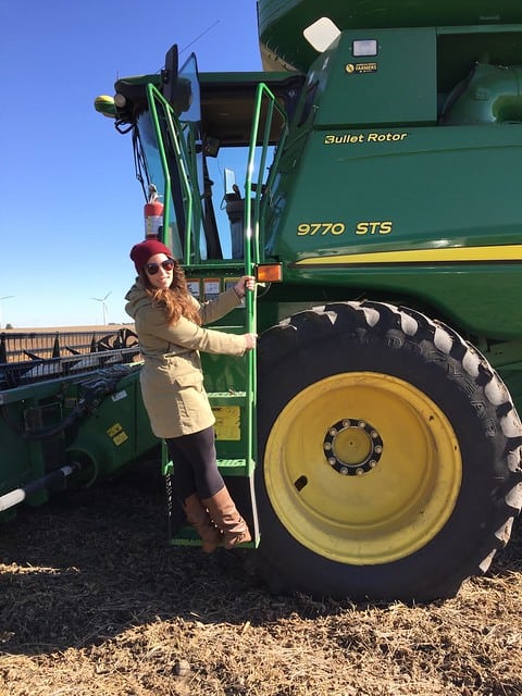 Blog author standing on a ladder on the side of a green harvester