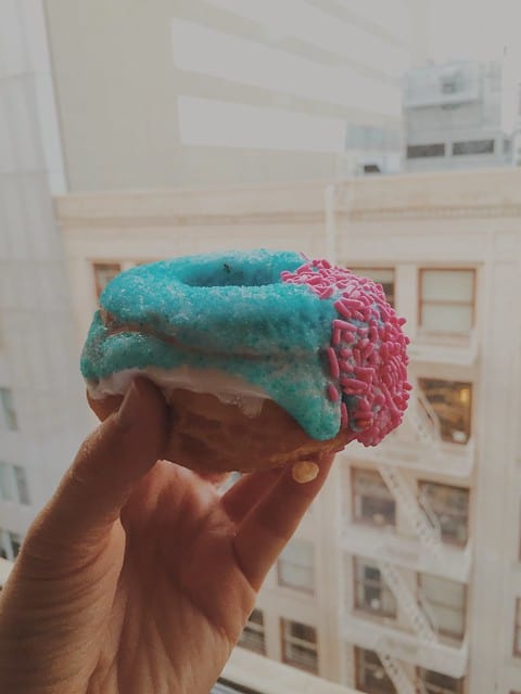 Close-up of a hand holding a blue and pink Voodoo donut