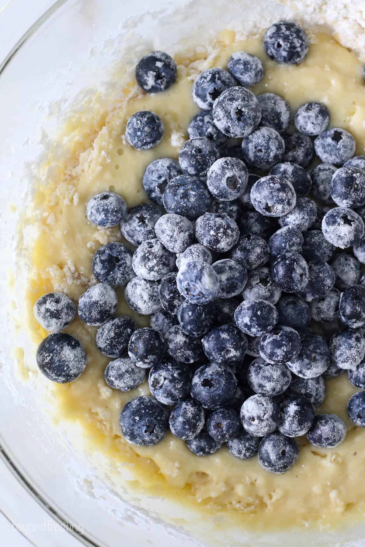 a glass mixing bowl of bread batter with floured blueberries