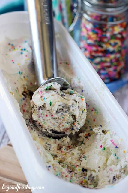 overhead of a scoop of cake batter cookie dough ice cream being scooped out of an ice cream tub