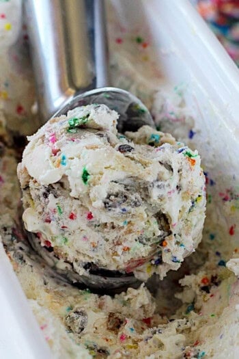 Overhead view of birthday cake ice cream being scooped out of an ice cream tub with an ice cream scoop.