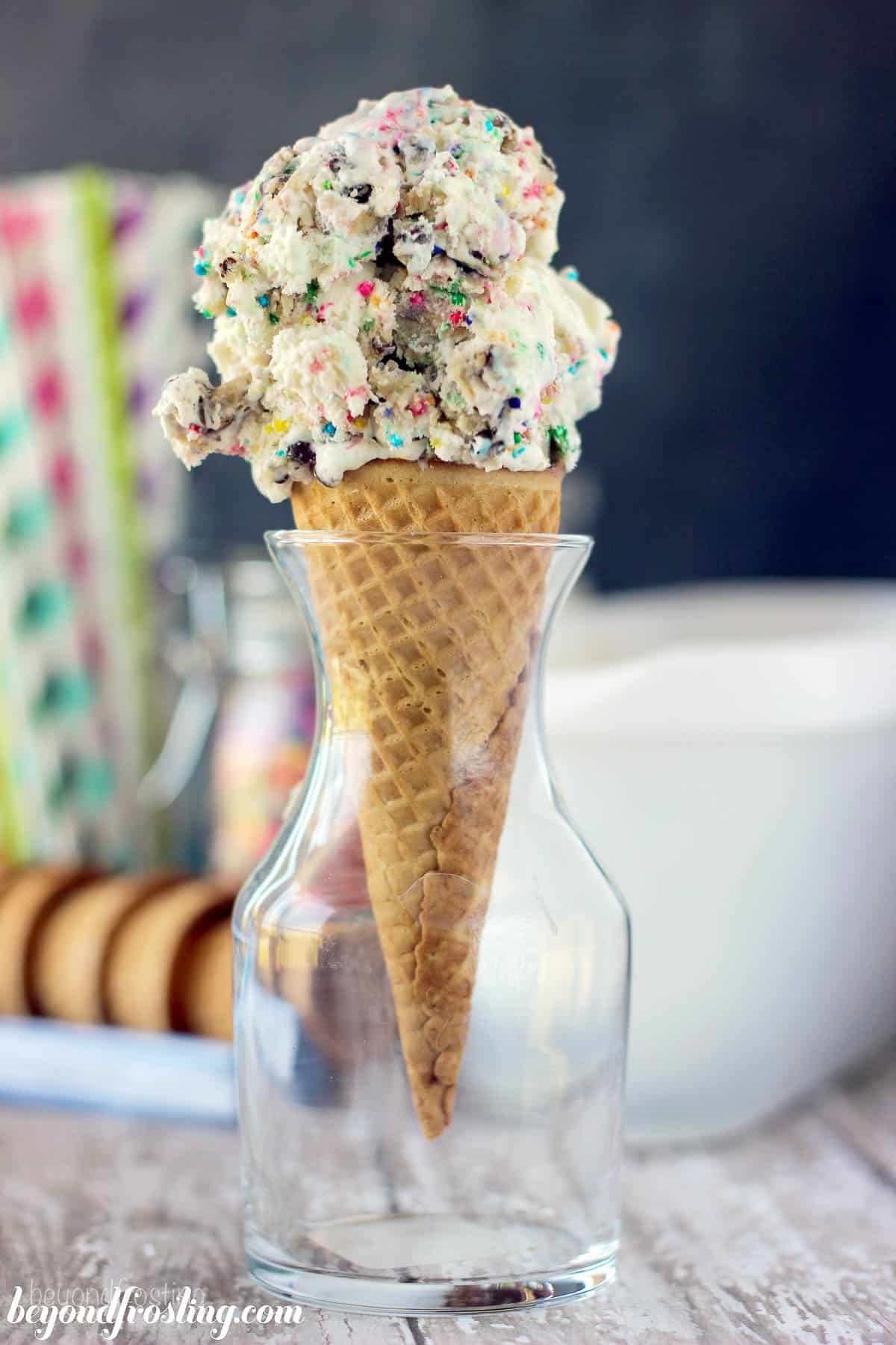 an ice cream cone set in a glass vase piled with a scoop of cookie dough ice cream