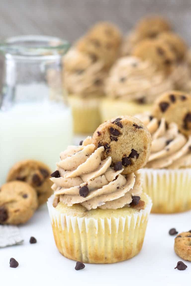 A close up of a frosted cupcake with a mini chocolate chip cookie on top and mini chocolate chips
