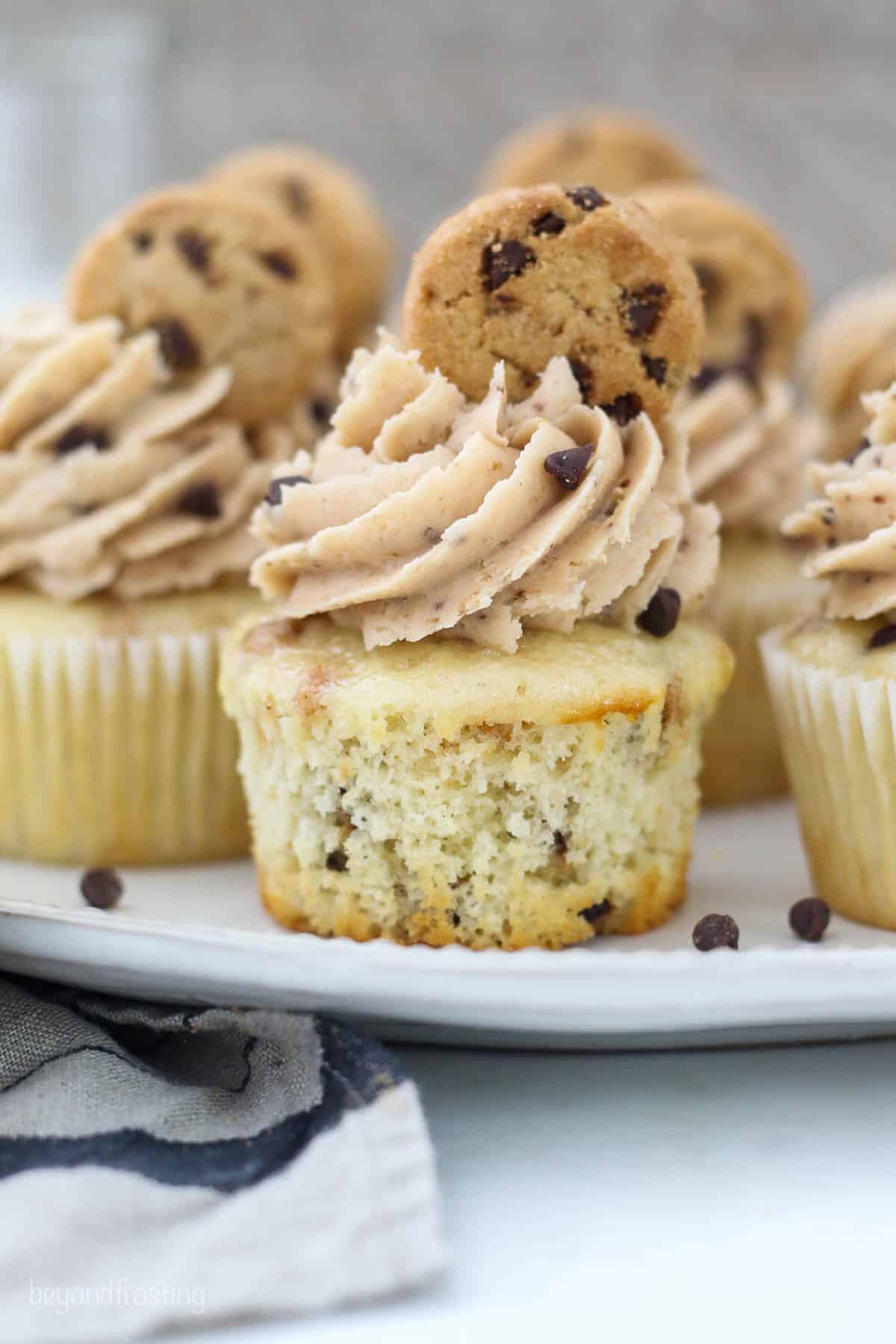 A close up of an unwrapped cupcake with frosting and topped with a mini chocolate chip cookie