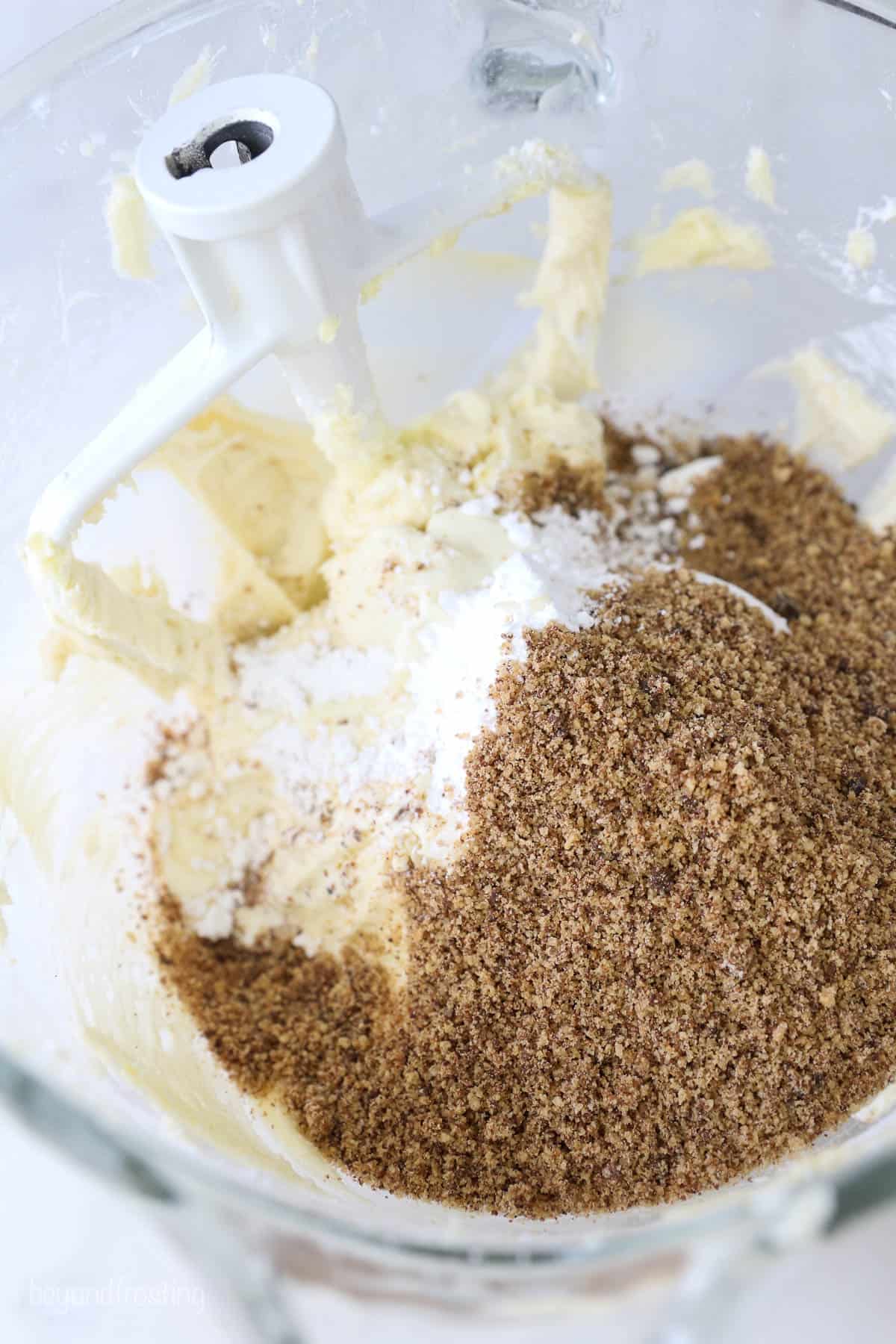 A glass mixing bowl of frosting with powdered sugar and chocolate chip cookie crumbs