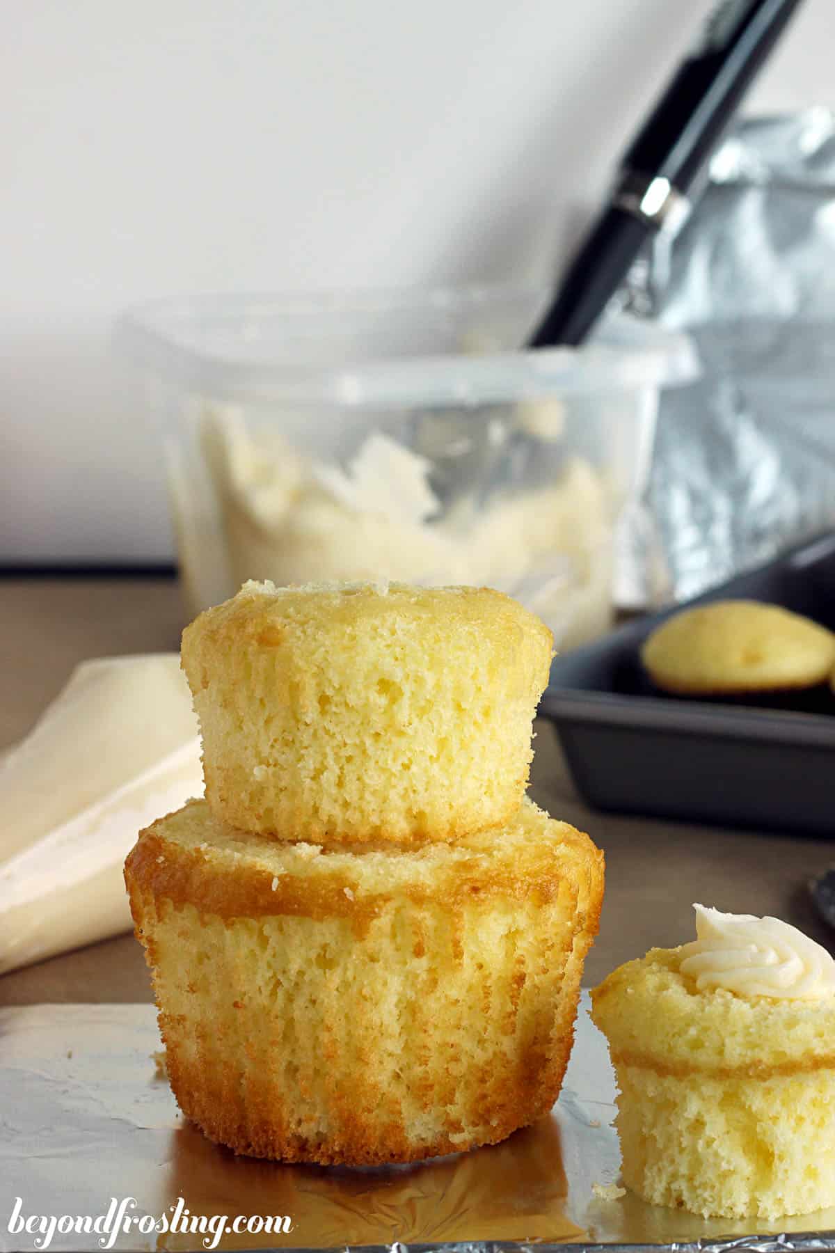 two cupcakes stacked with a container of frosting in the background