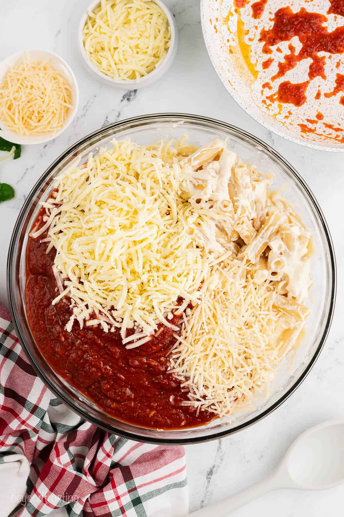 Ziti pasta, shredded cheese, and pasta sauce in a bowl
