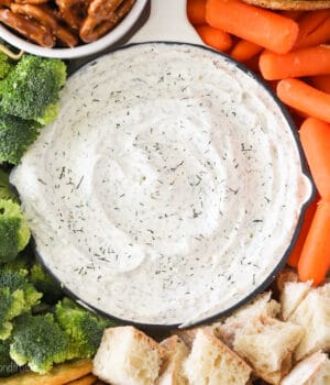 Close up of a bowl of dill dip with broccoli, carrots, bread and pretzels