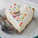 slight overhead front view of a slice of funfetti pie on a white plate next to two forks