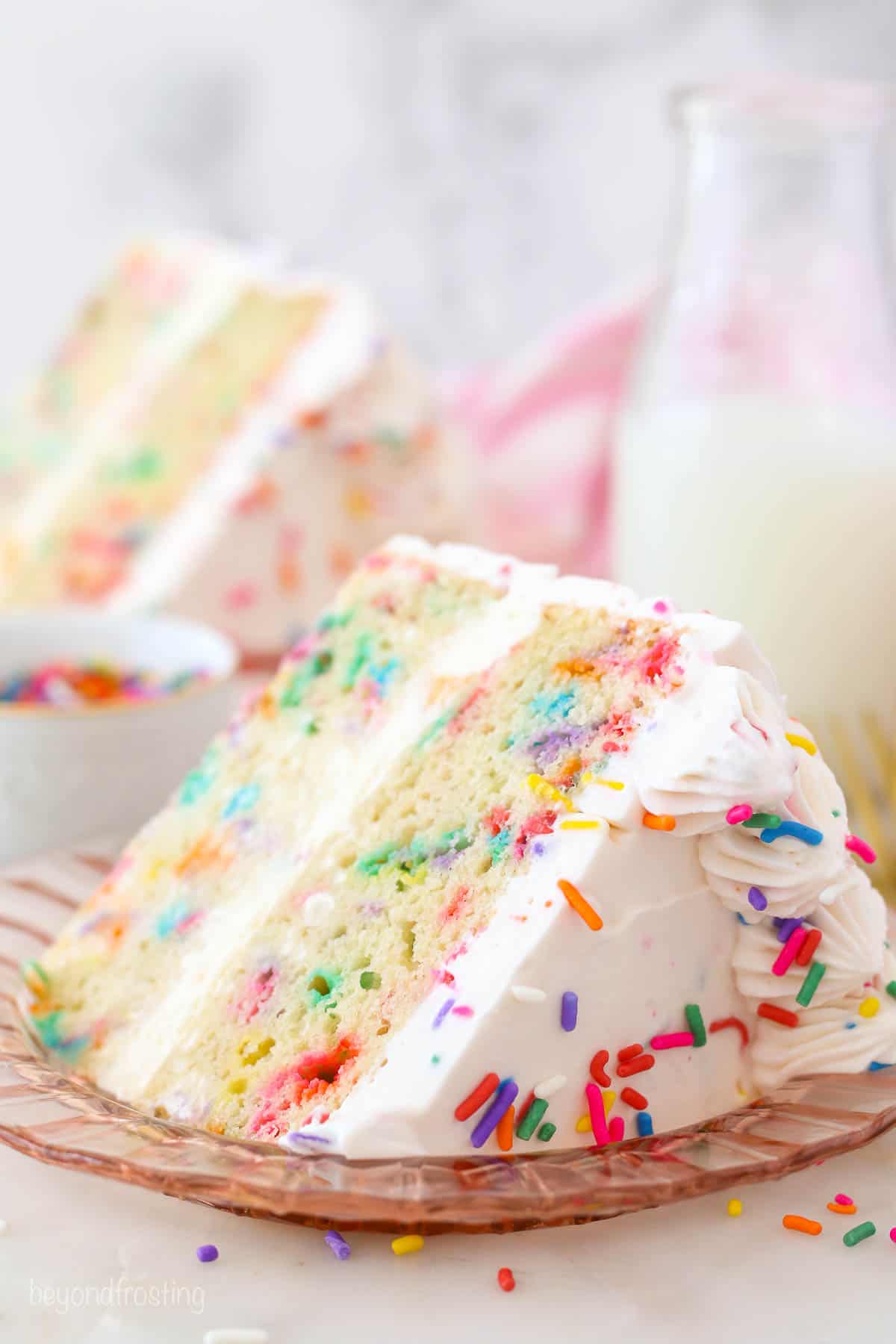 A close up of a slice of Funfetti Ice cream cake on a pink plate with sprinkles
