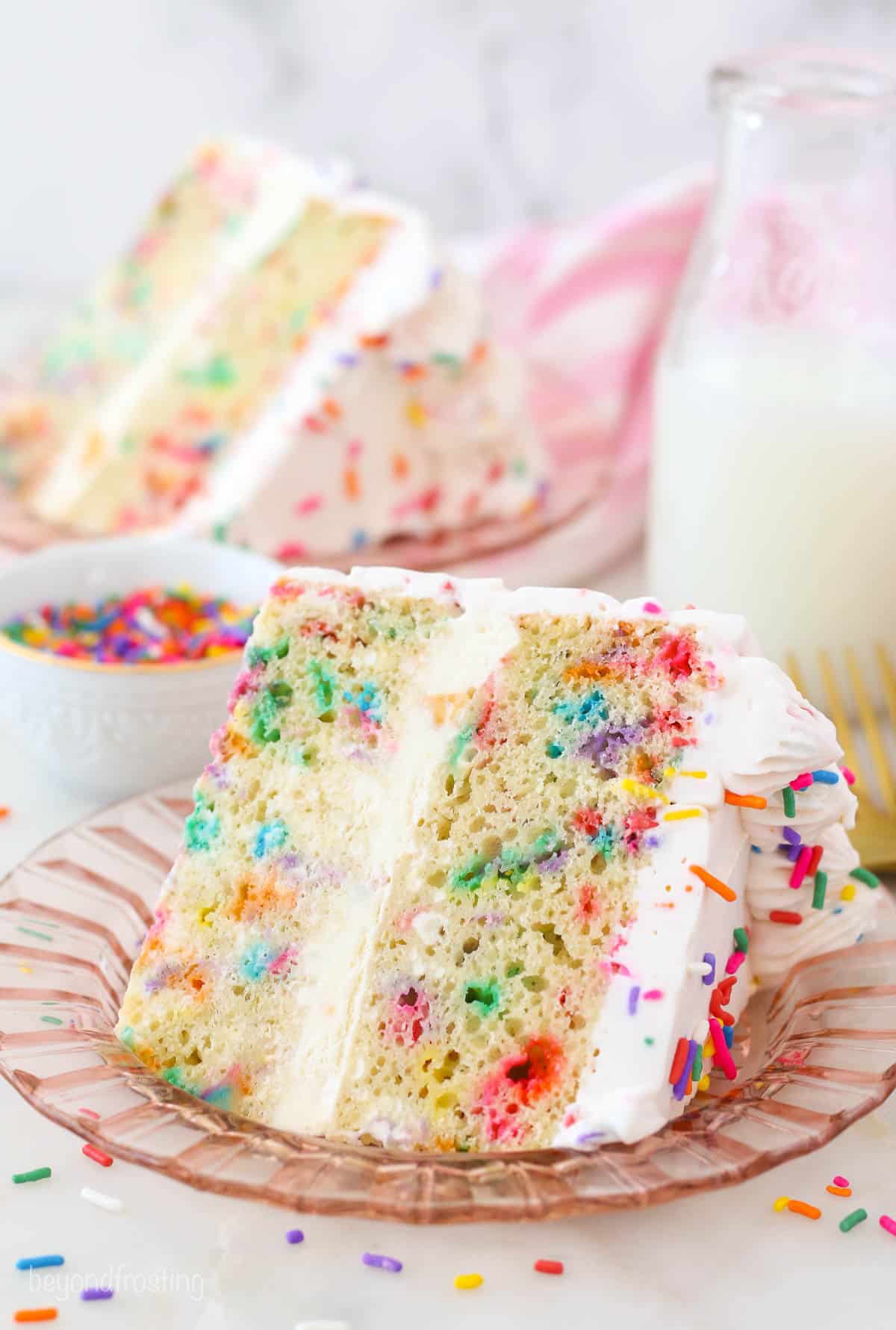 A slice of Funfetti ice cream cake on a pink plate, a small bowl of sprinkles and a glass of milk
