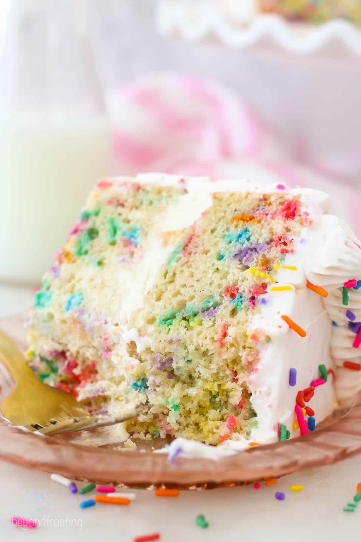 A slice of Funfetti ice cream cake on a pink plate with bites missing