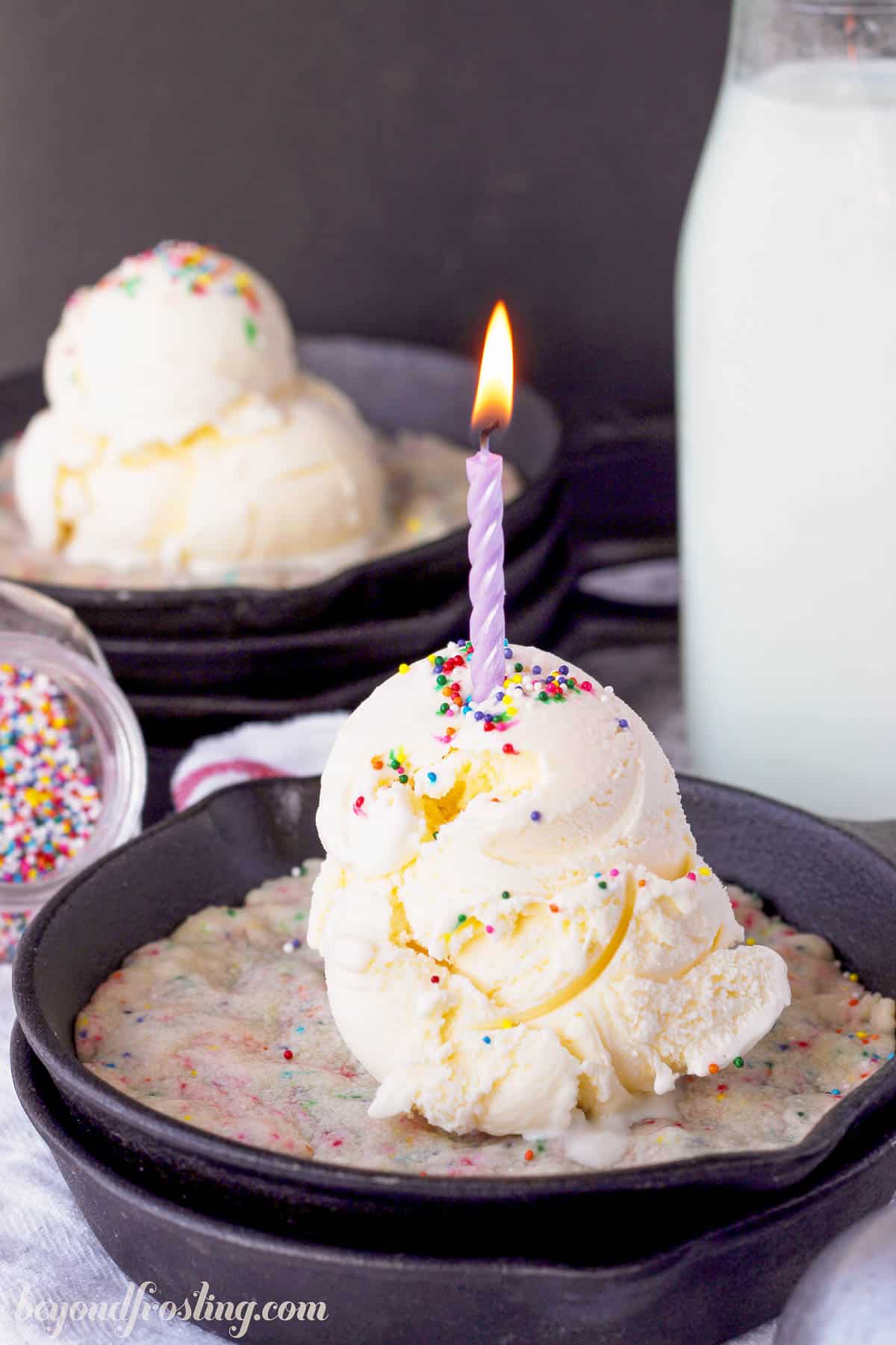 side view of a skillet cookie topped with a scoop of vanilla ice cream and a candle