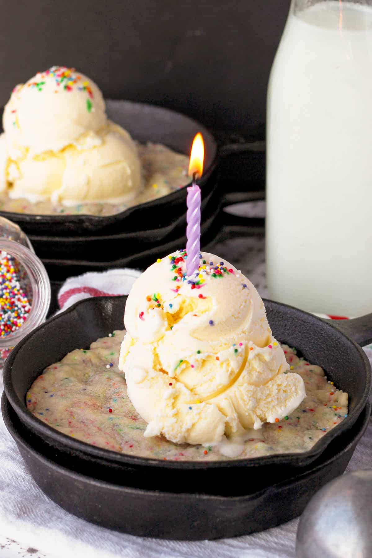 side view of a cookie in a skillet topped with a large scoop of vanilla ice cream