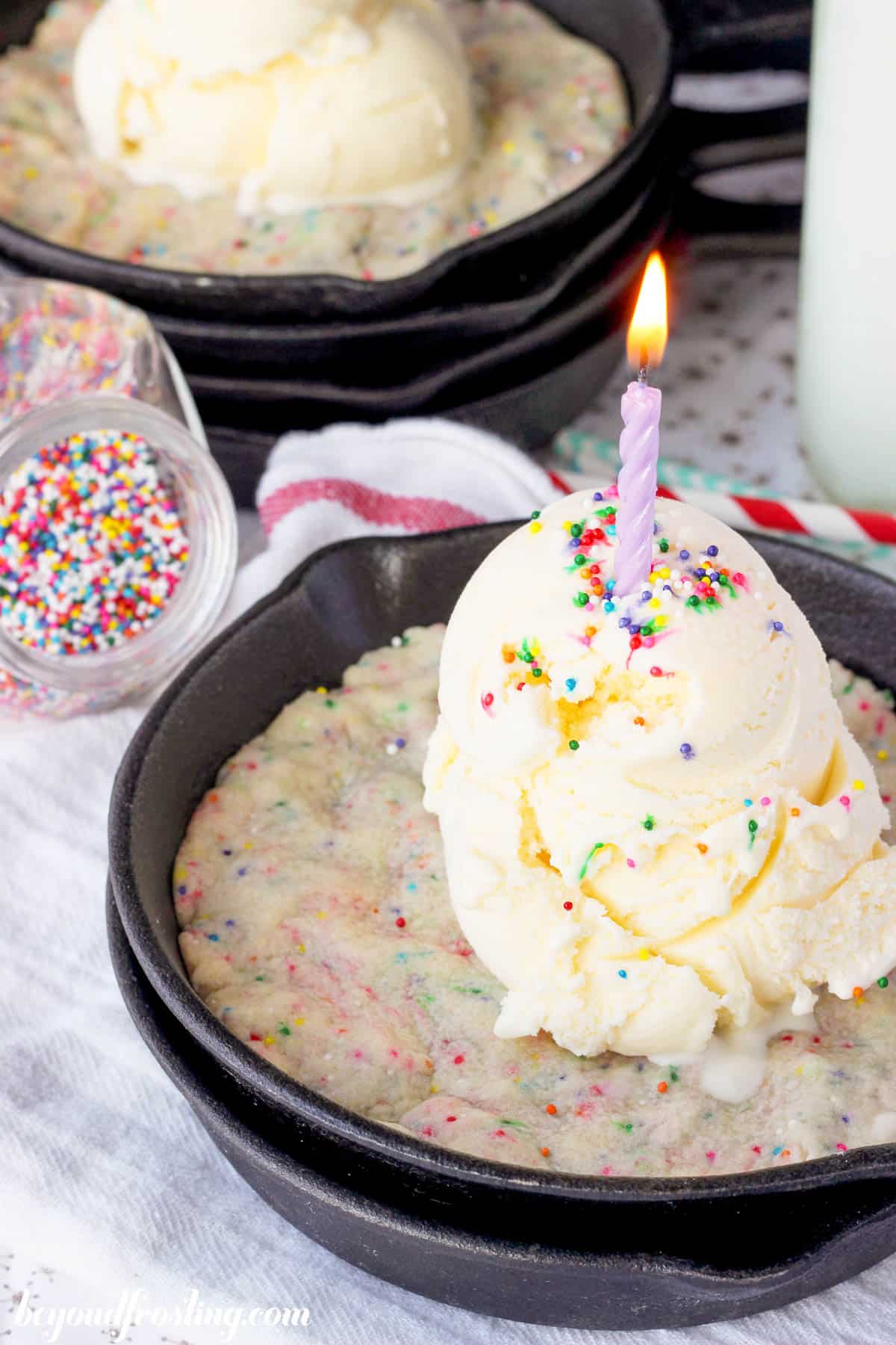 closeup of a skillet with a funfetti cookie topped with ice cream, sprinkles, and a candle