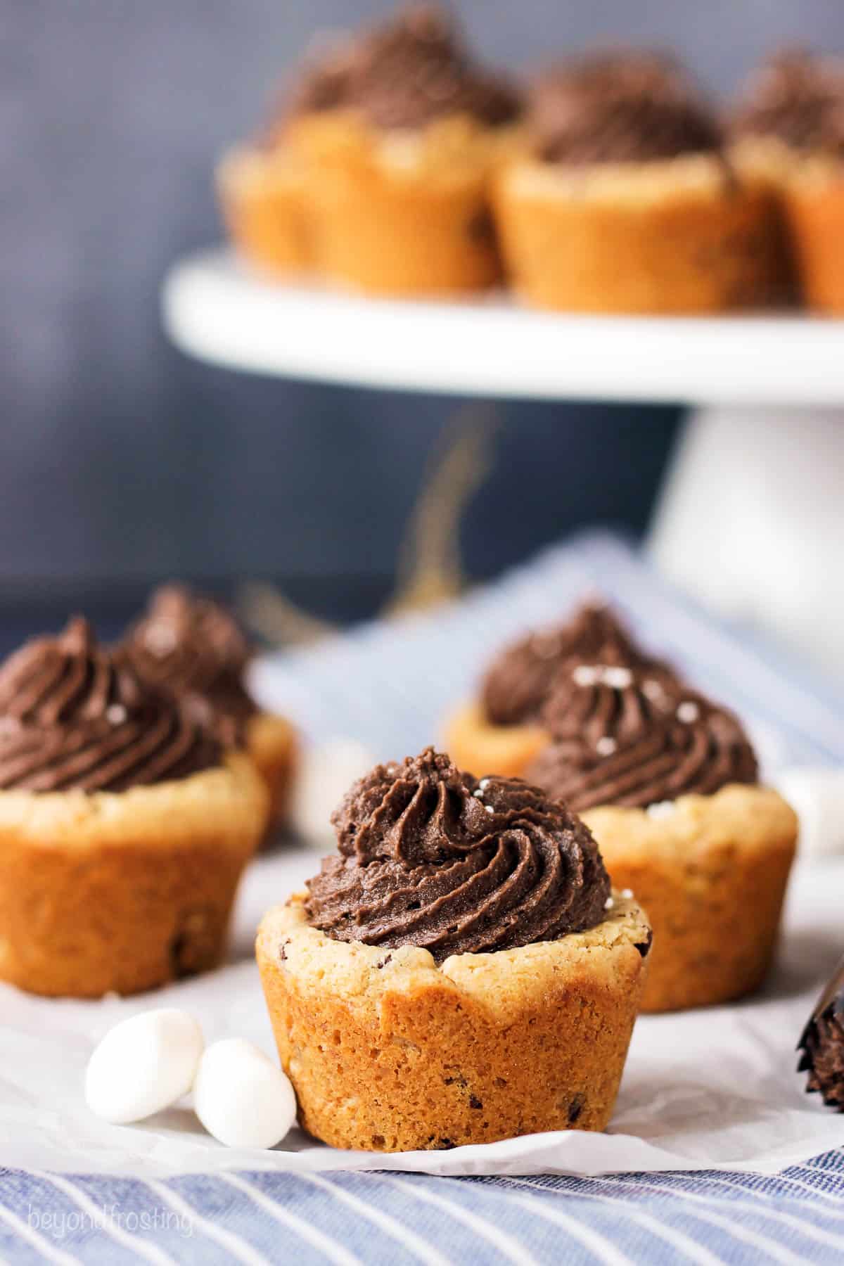 side view of graham cracker cookie cups on parchment paper with a cake stand full of cookie cups in the background