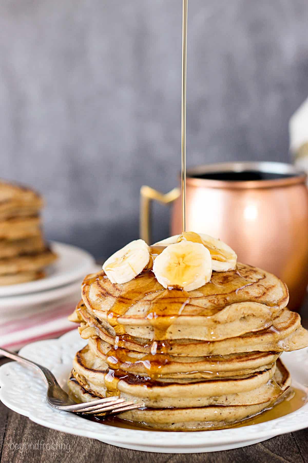 a stack of healthy peanut butter pancakes topped with banana slices being drizzled with maple syrup