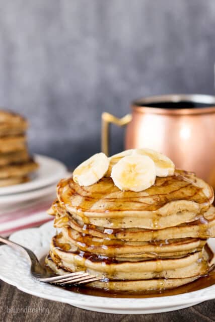 side view of a stack of pancakes topped with banana and maple syrup