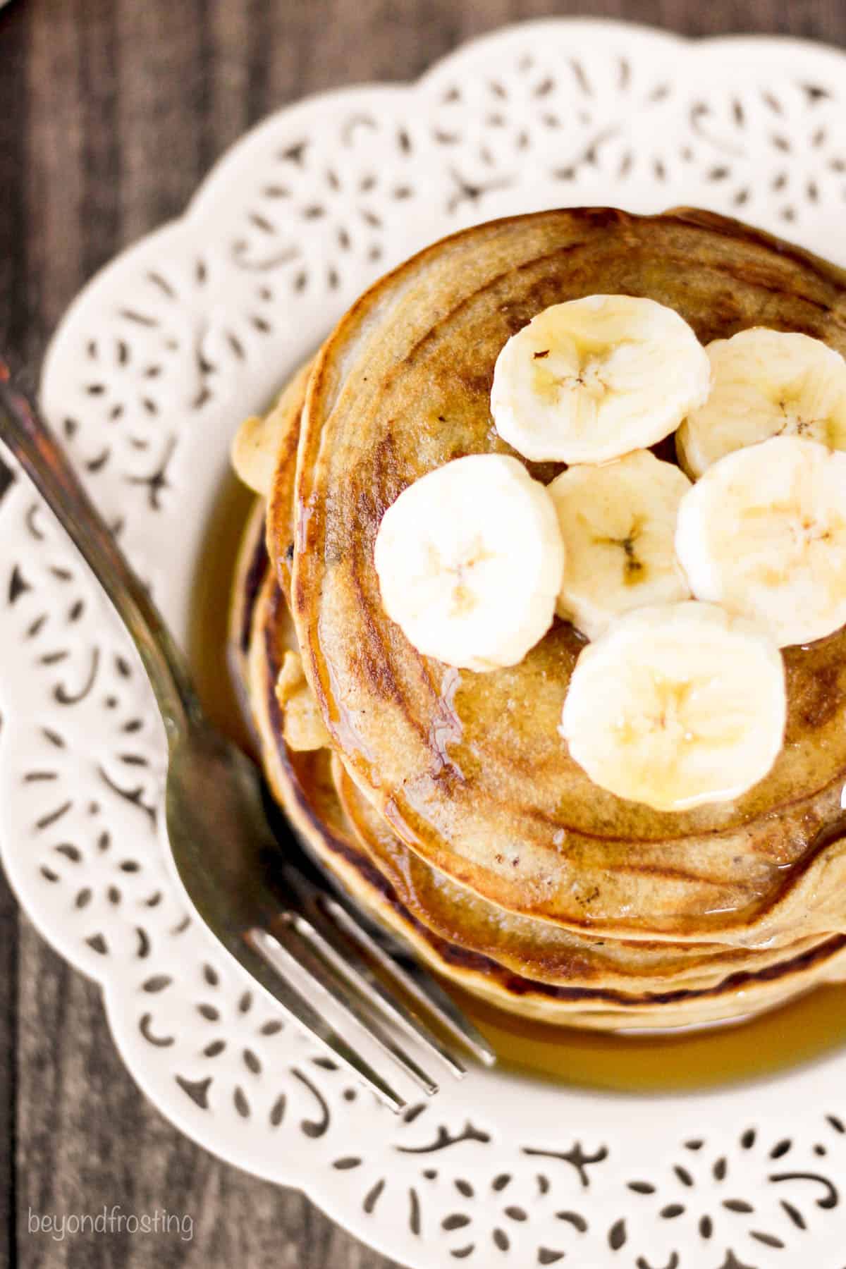 overhead of a stack of pancakes on a plate topped with banana slices