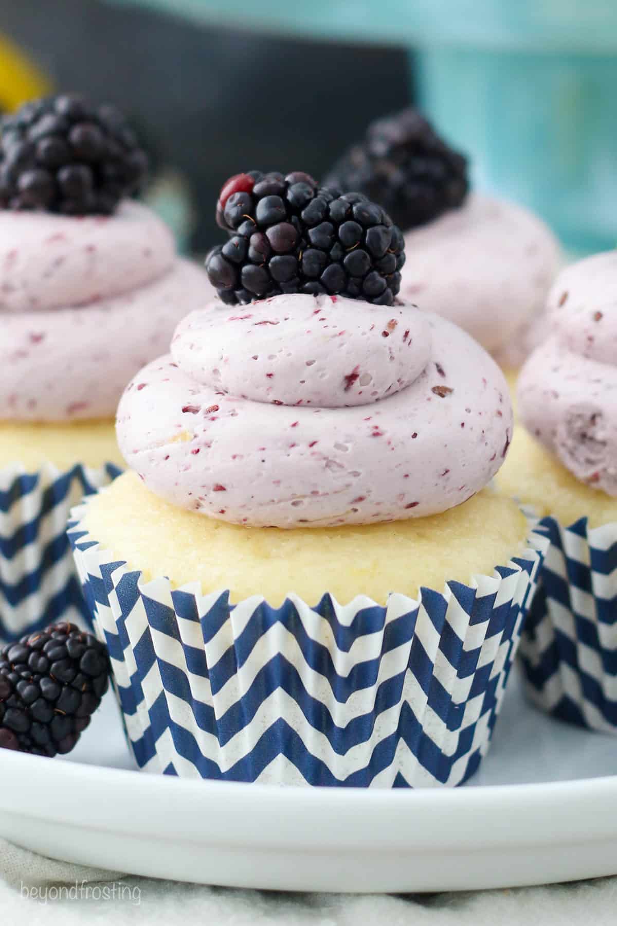 side view of a frosted lemon cupcake topped with blackberry frosting and a fresh blackberry