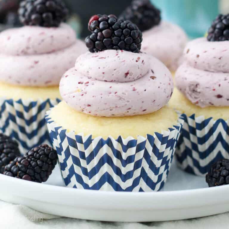 Closeup of a lemon blackberry cupcake on a plate surrounded by more cupcakes.
