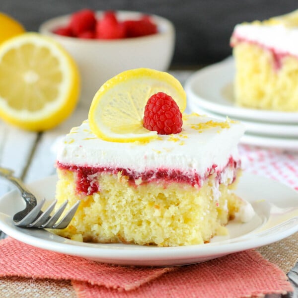 closeup of a square slice of lemon cake on a plate garnished with fresh raspberry and a lemon slice