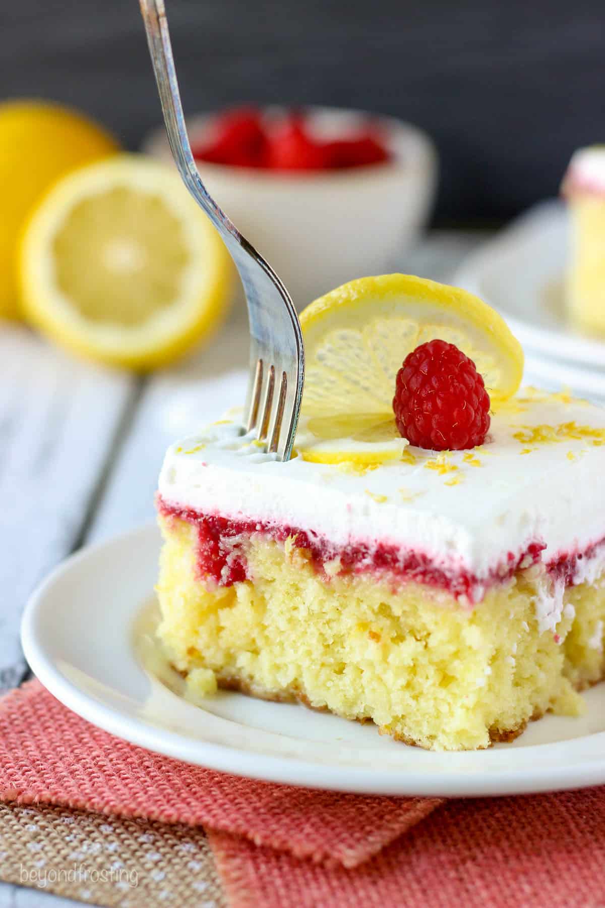 a fork being plunged into a slice of lemon poke cake on a white plate