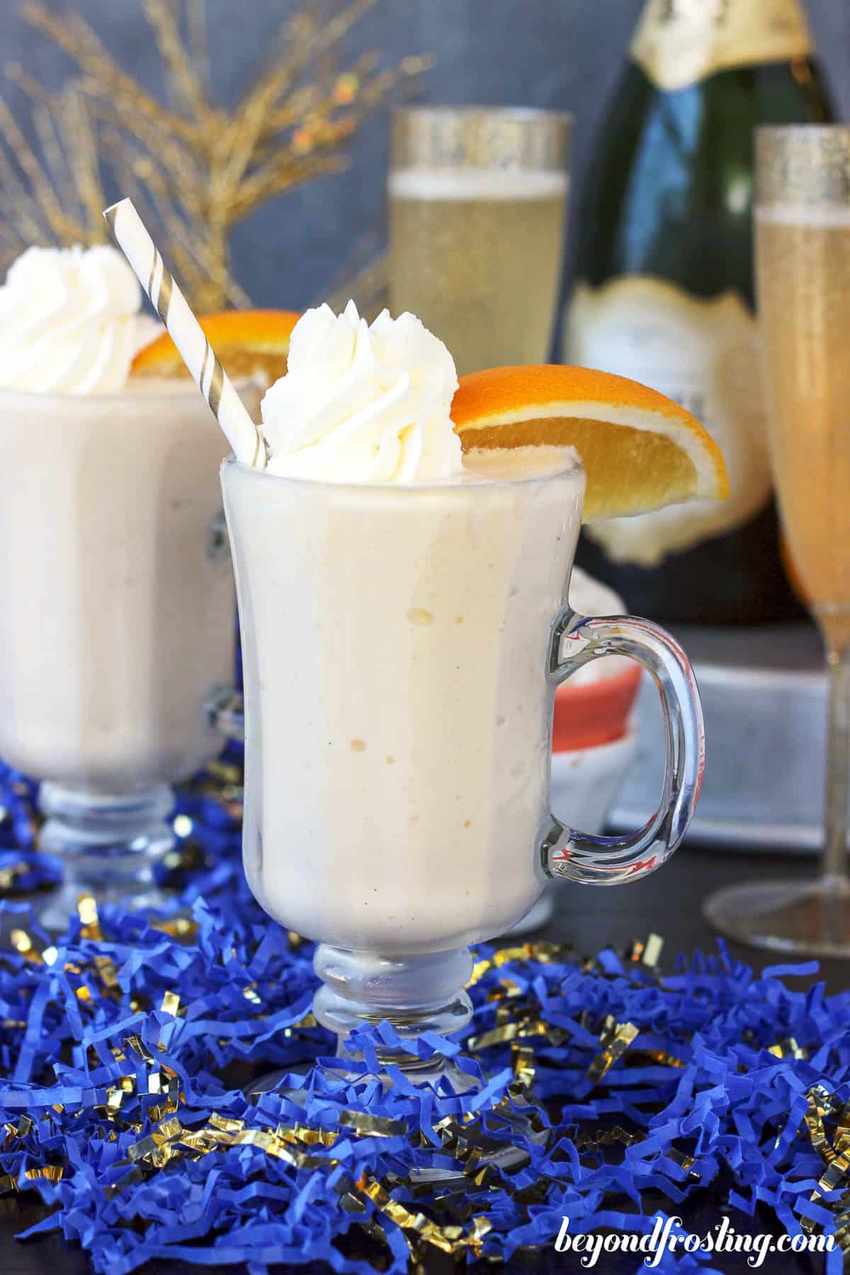 side view of two mimosa milkshakes topped with whip and garnished with orange slices