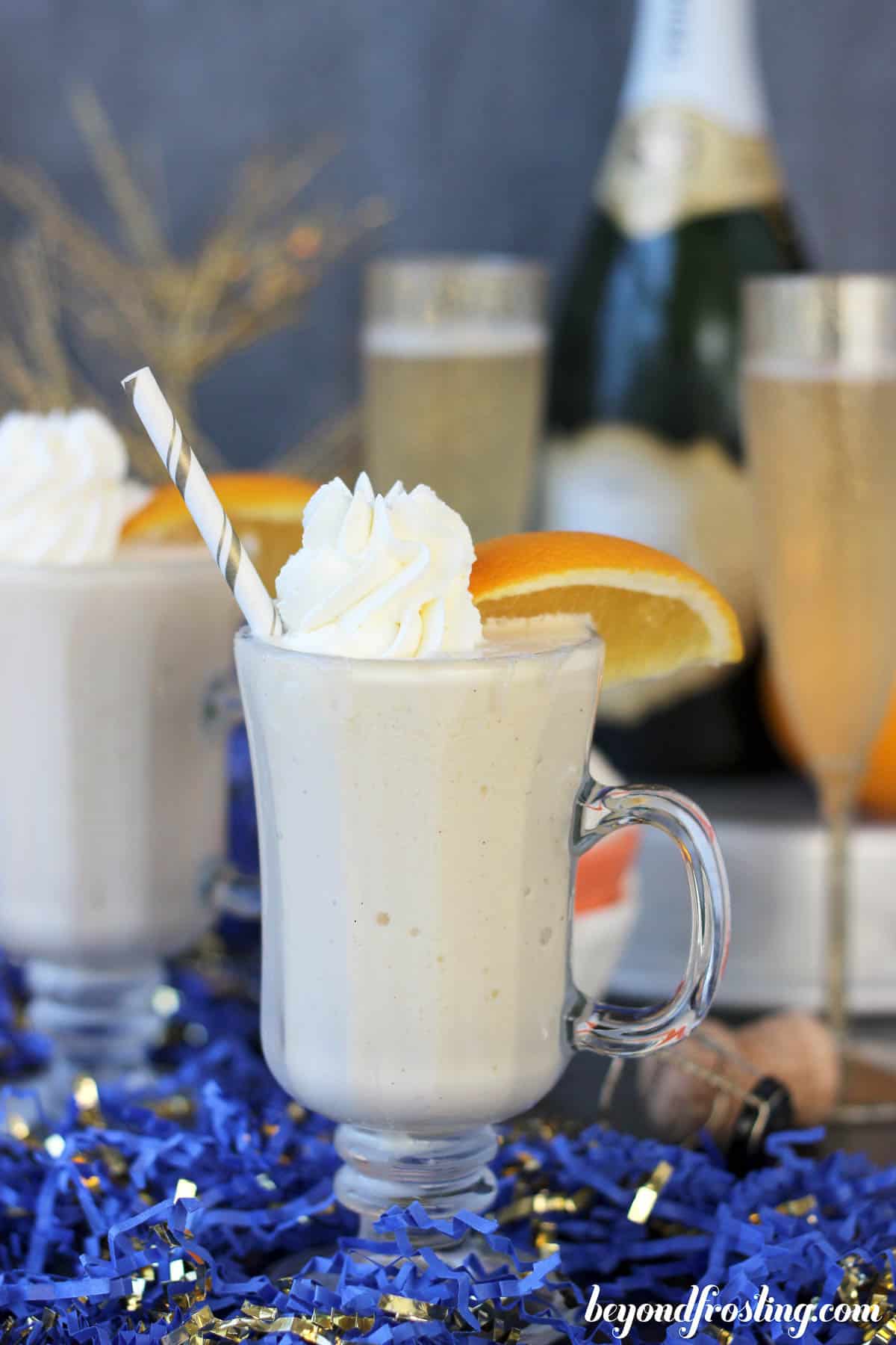 side view of two mimosa milkshakes with champagne in the background