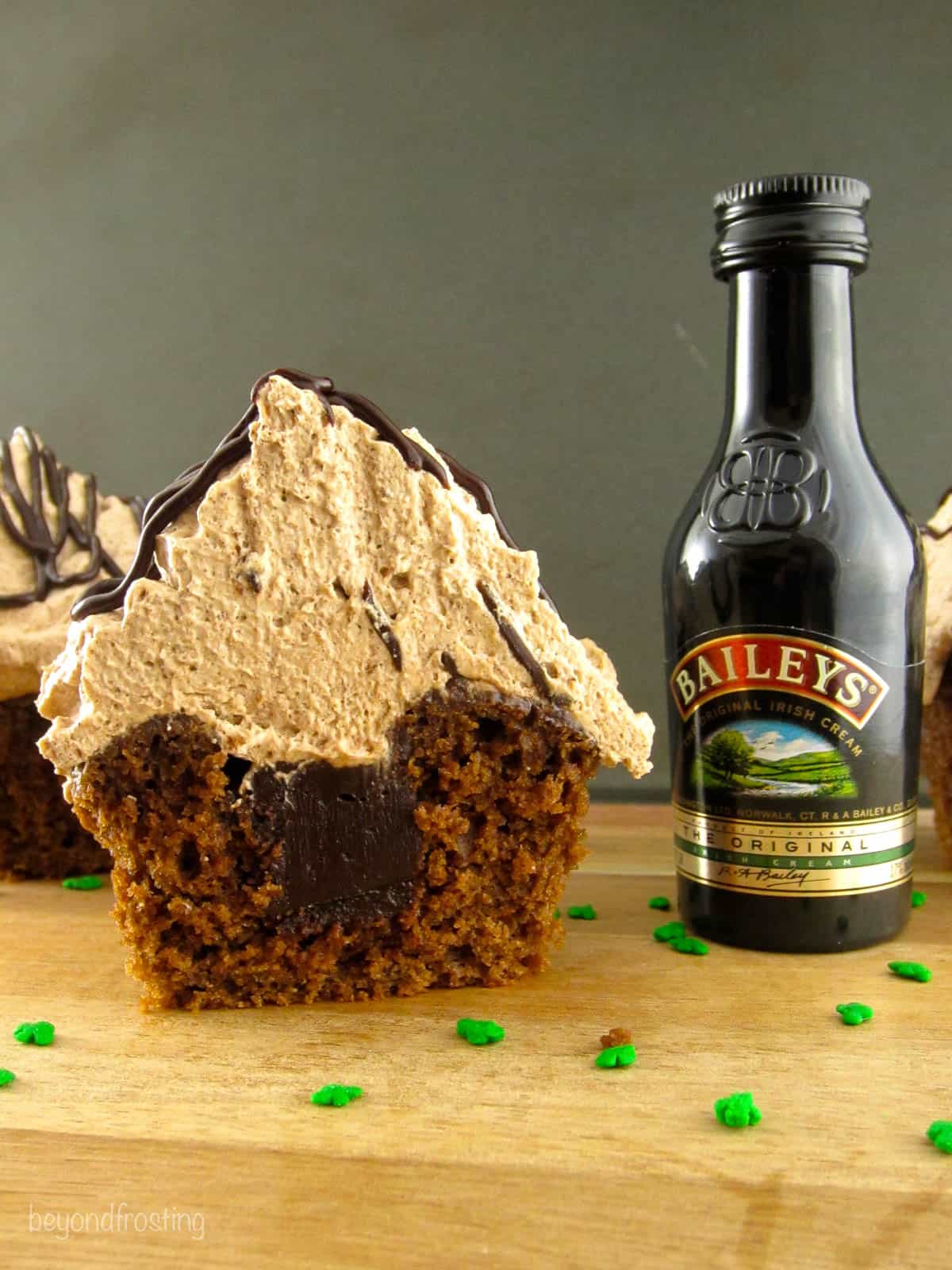 side view of an irish cream cupcake cut in half and set next to a small bottle of Baileys