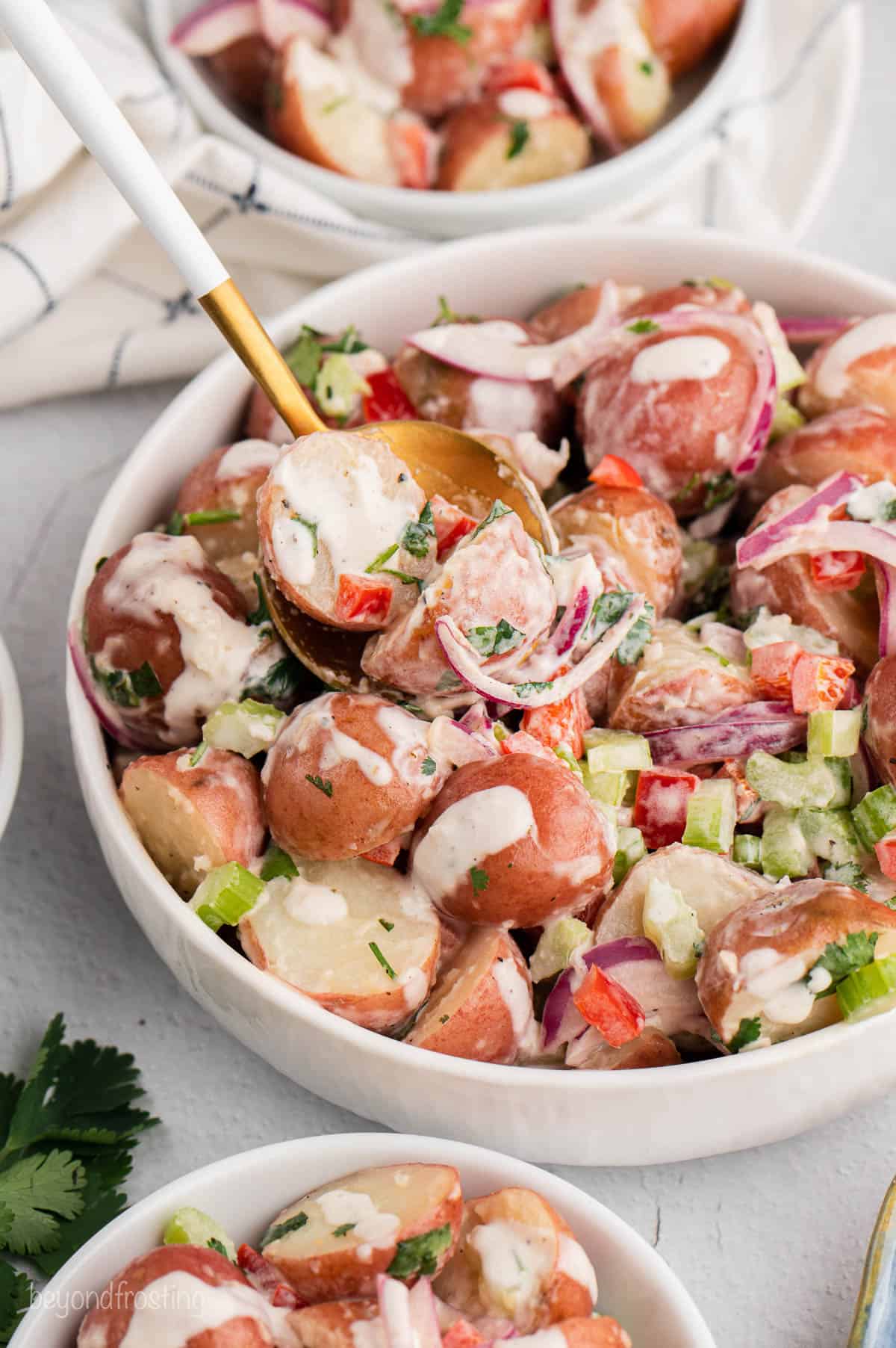A gold spoon in a big bowl of red potato salad