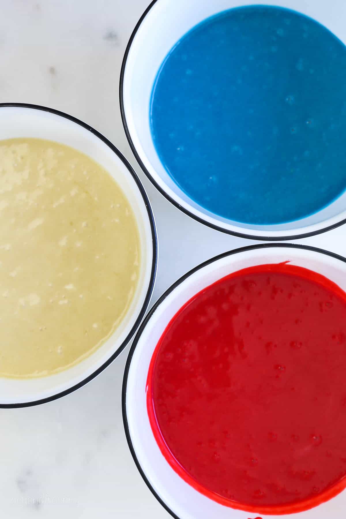 three bowls of cake batter, one is white, one is blue and one is red