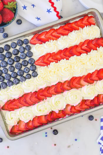 overhead view of an American Flag cake decorated with blueberries, strawberries and whipped cream