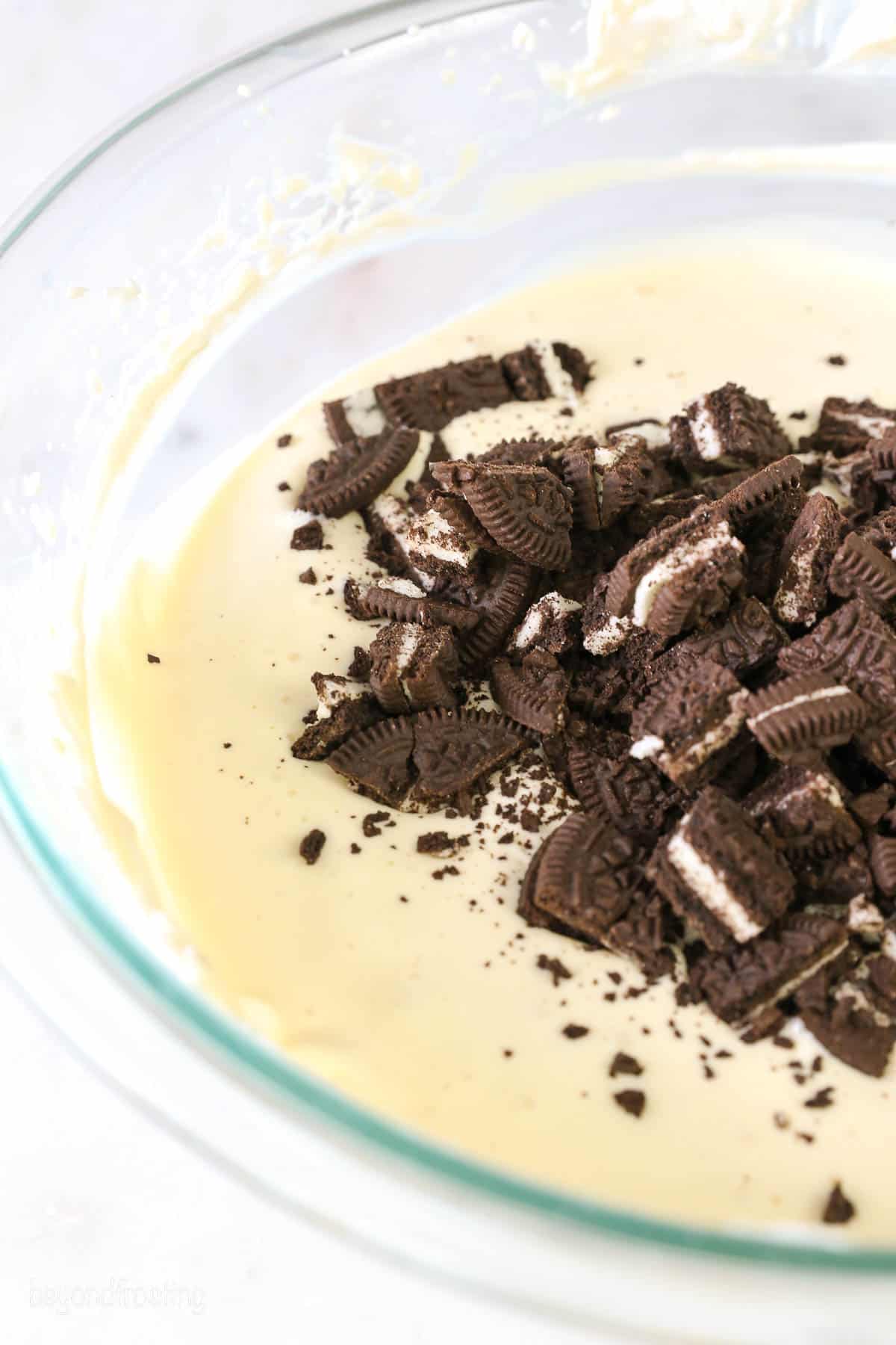 a glass mixing bowl of cheesecake batter with crushed Oreos