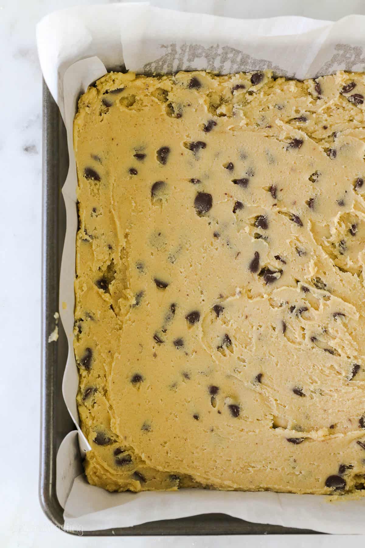 a cropped view of a 9-inch square pan with a layer of chocolate chip cookie dough