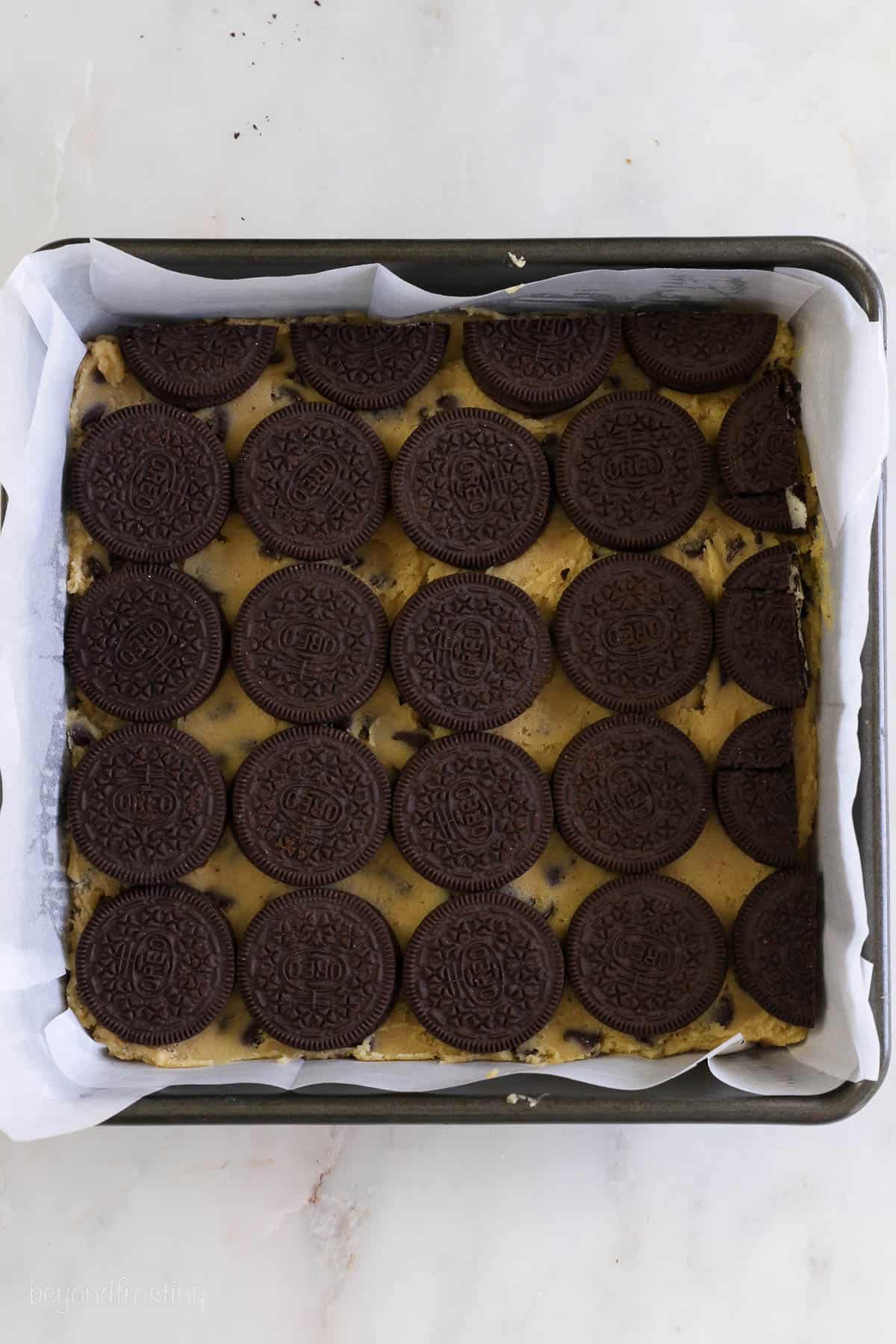 a 9-inch square pan with a layer of chocolate chip cookie dough and Oreos