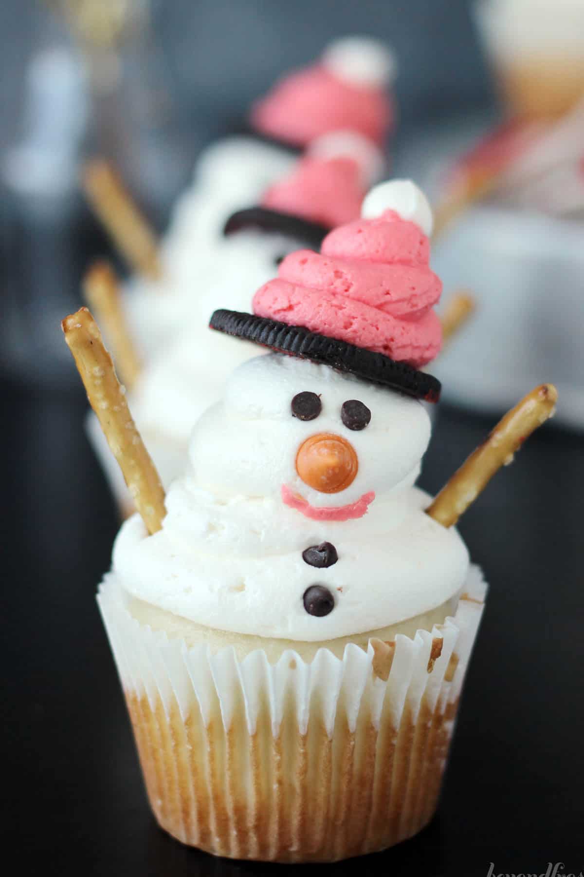 a front to back lineup of snowman cupcakes with one at the front in focus