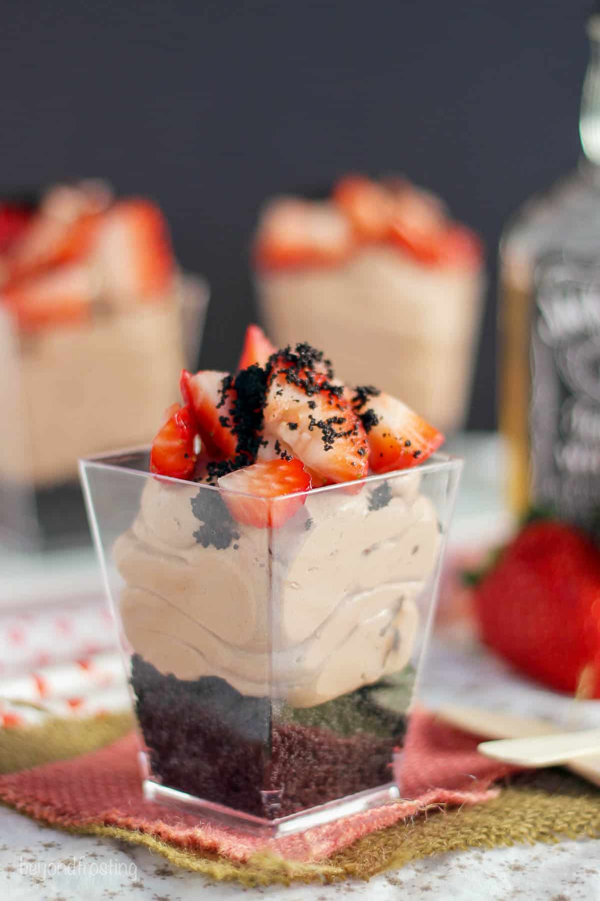 side view of a no-bake spiked parfait with two more parfaits and a bottle of whiskey in the background