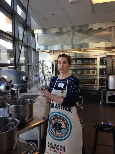 Blog author holding a giant stand mixer whisk in an industrial kitchen