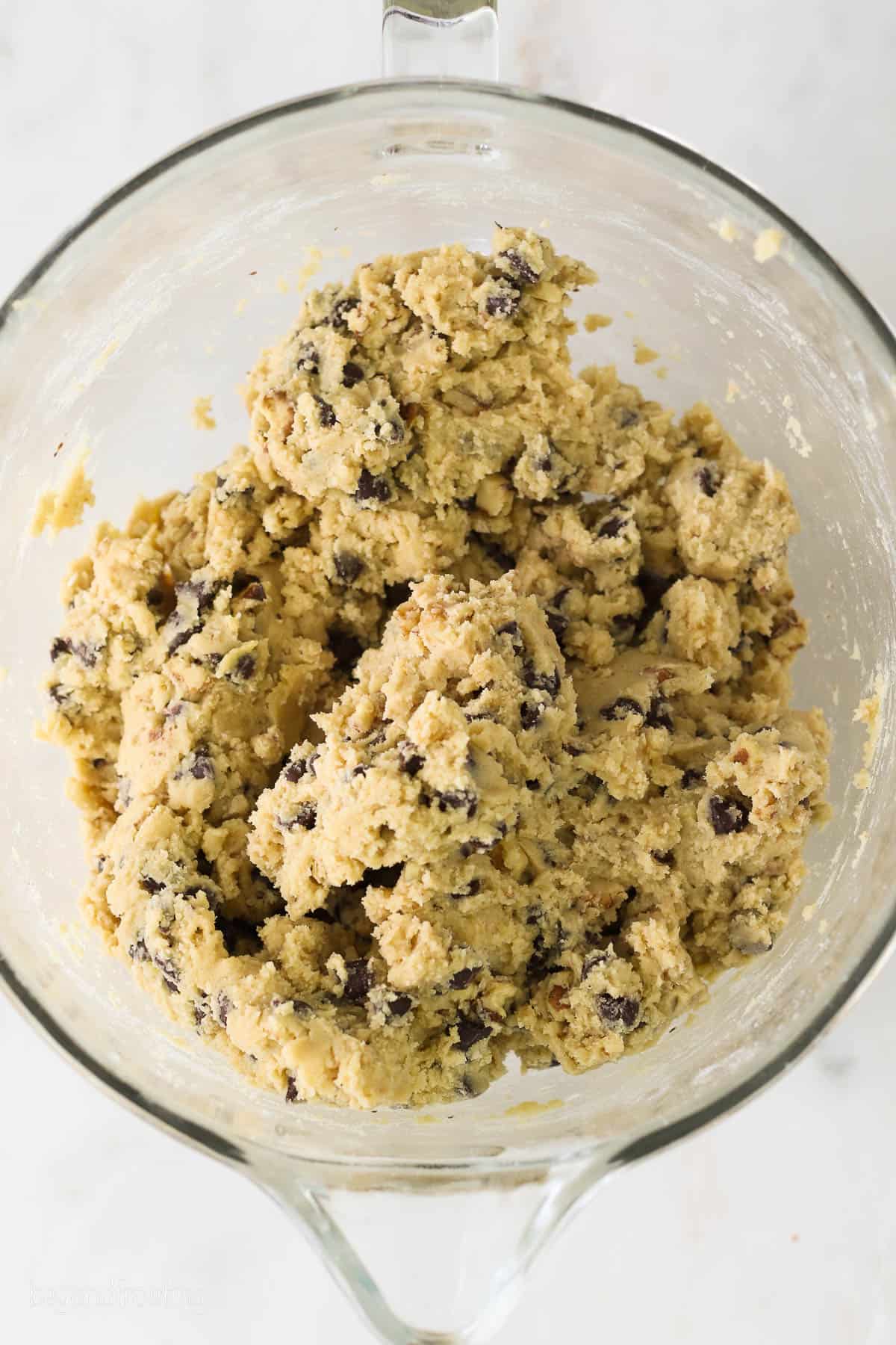 A glass mixing bowl with cookie dough for chocolate chip walnut cookies