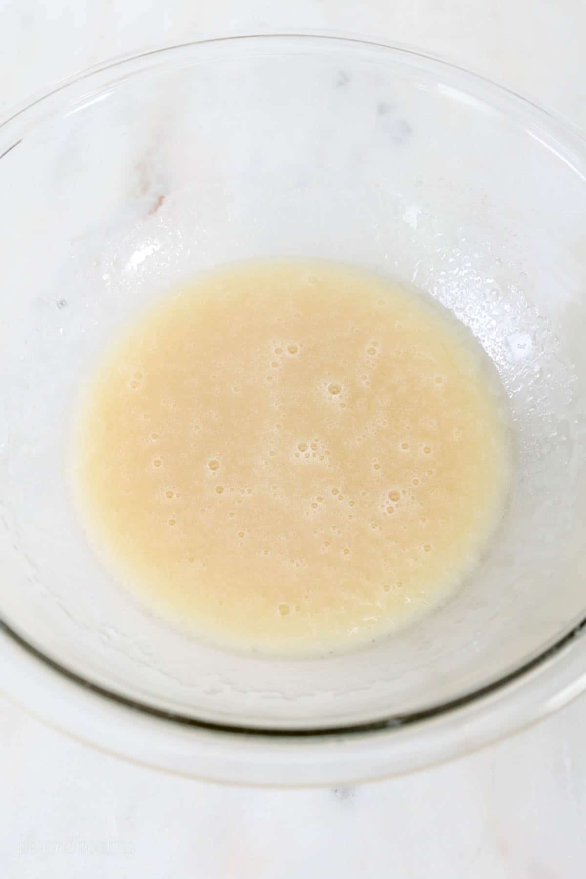 overhead of glass mixing bowl with beaten oil and sugar