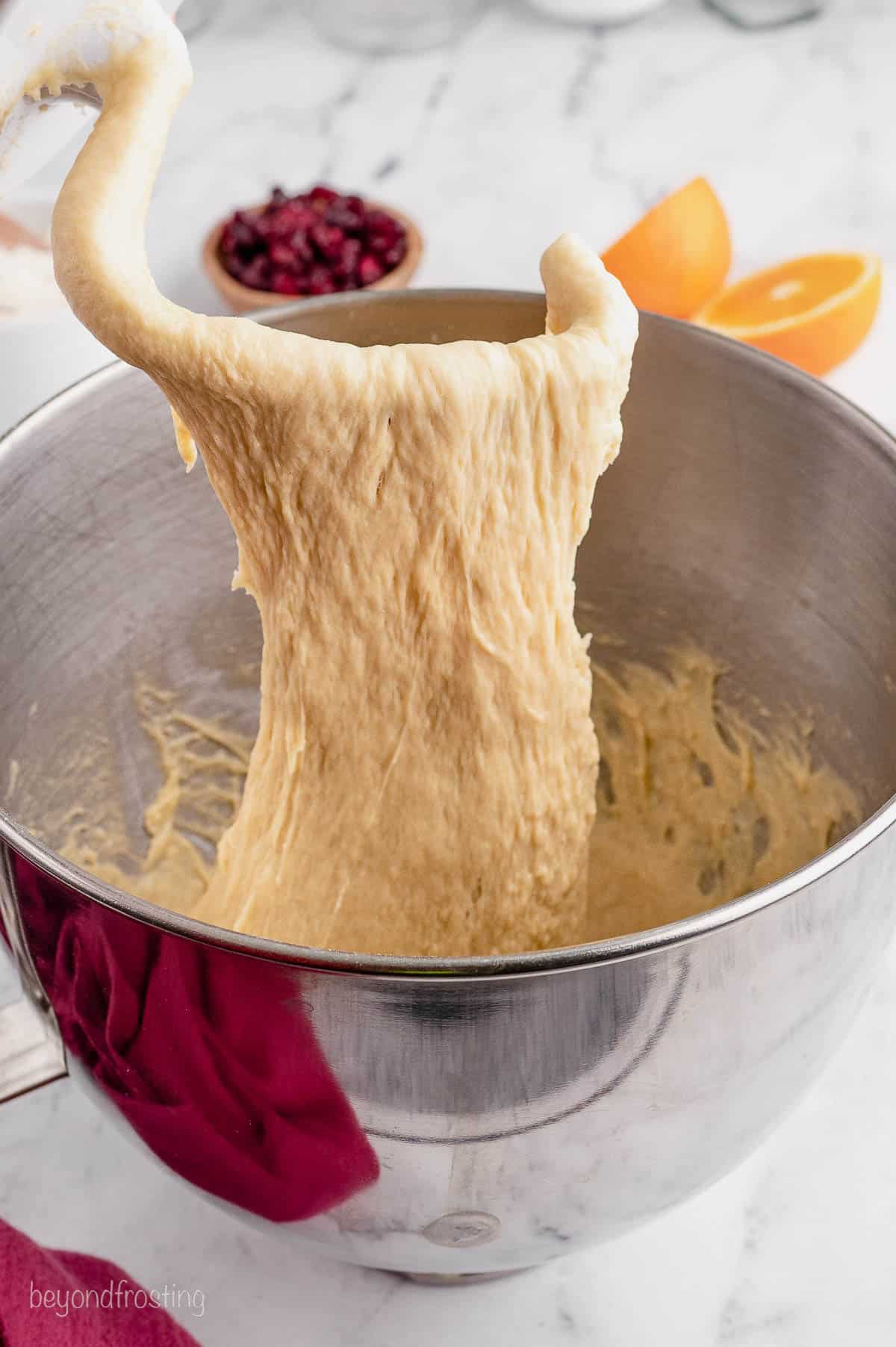 bread dough being lifted out of a mixing bowl