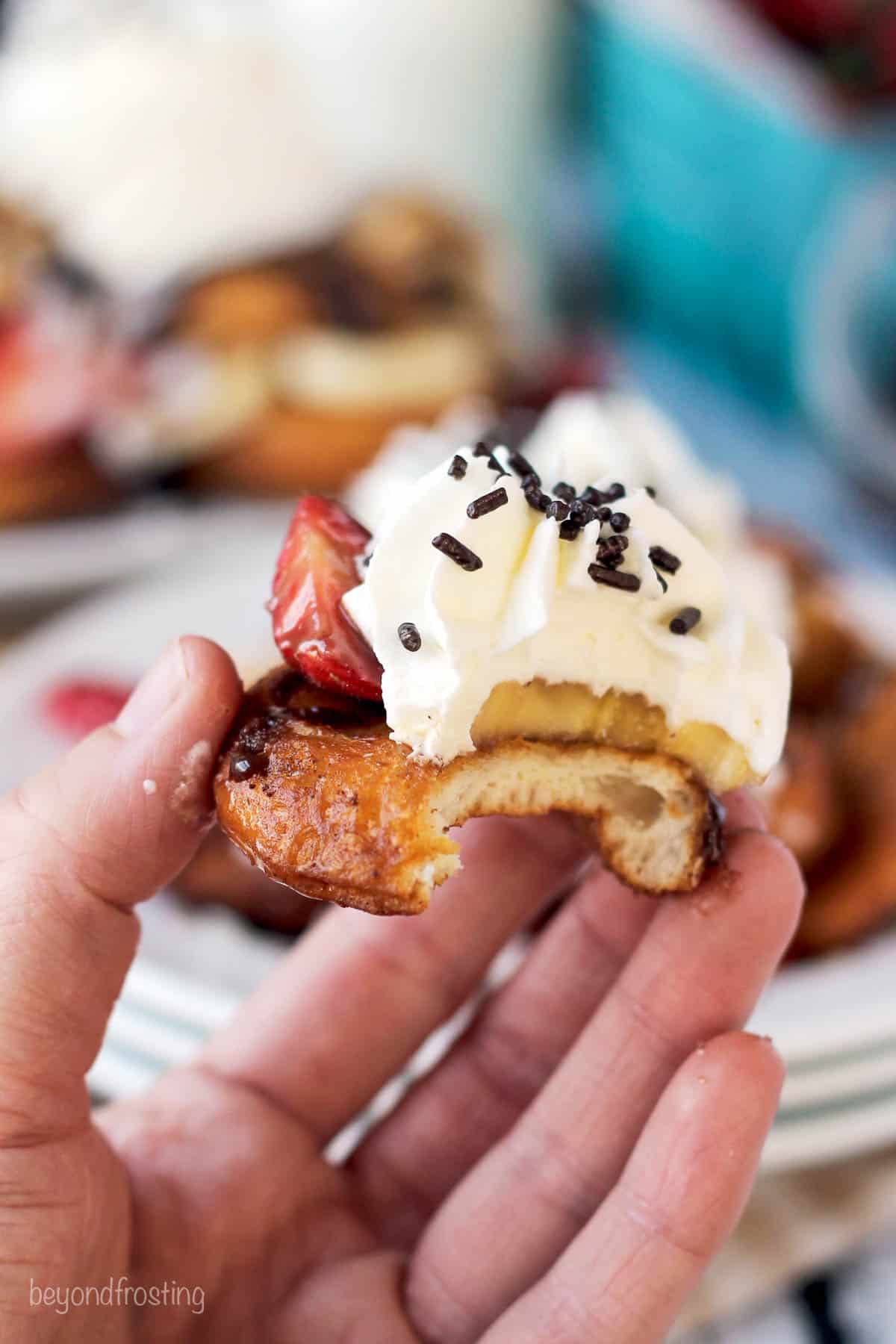 mini donut topped with whipped cream with a bite taken out held