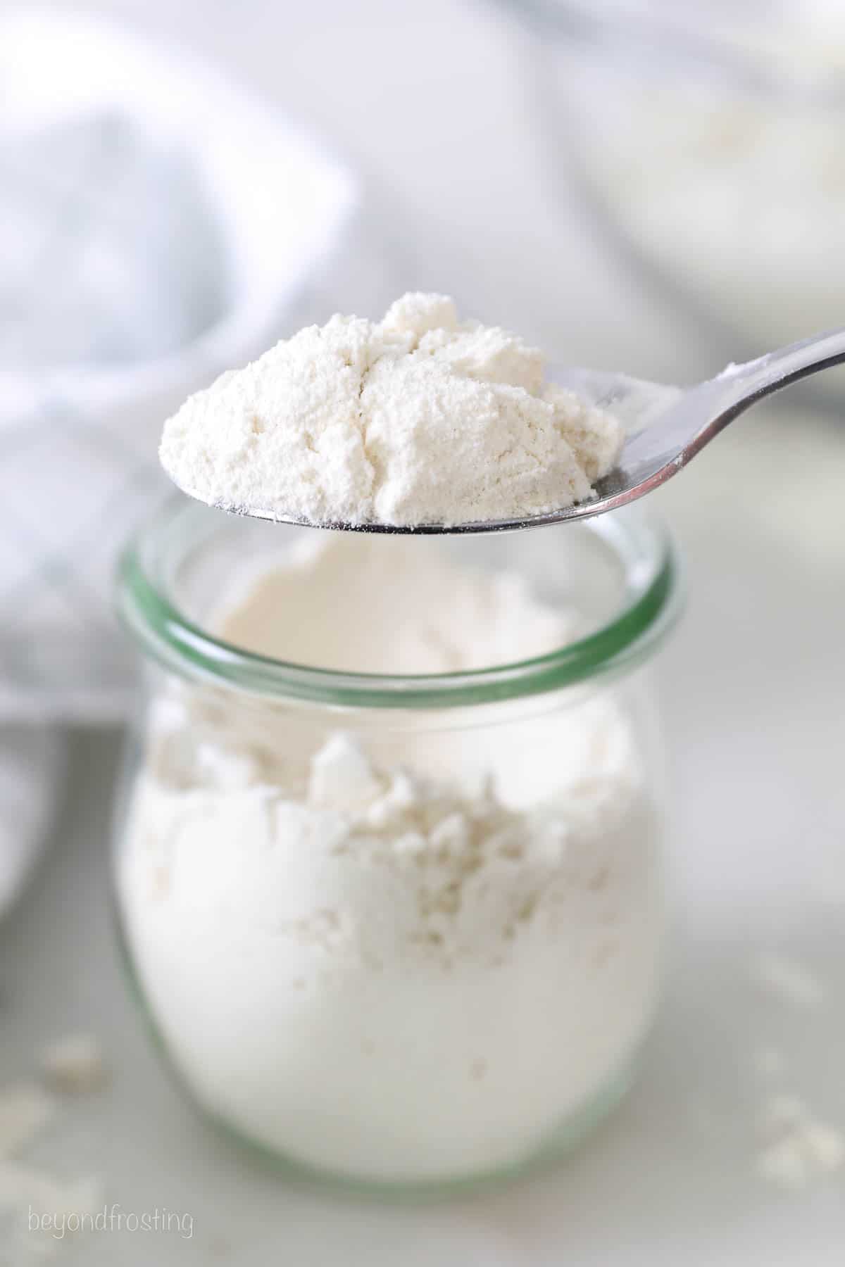 A spoonful of flour over a small jar of flour