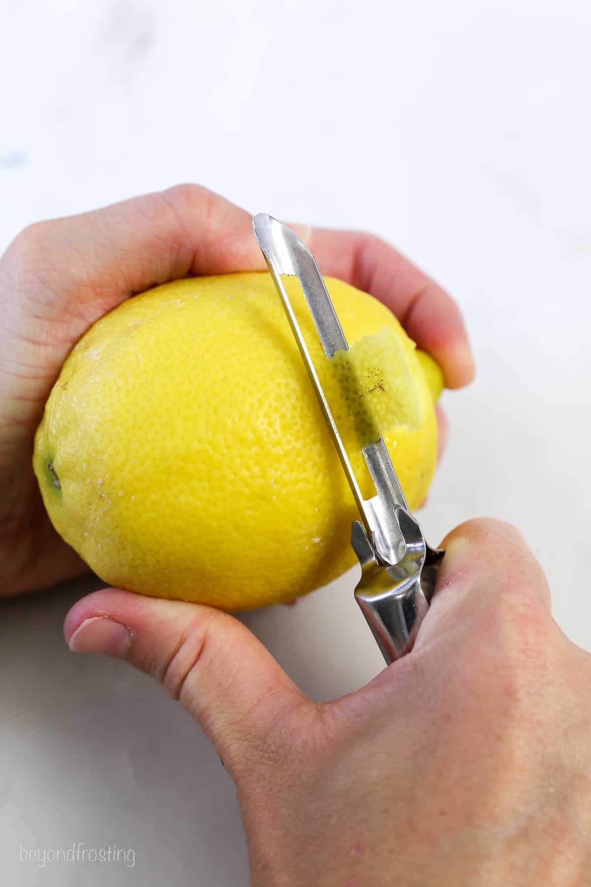 A vegetable peeler peeling the zest of a lemon