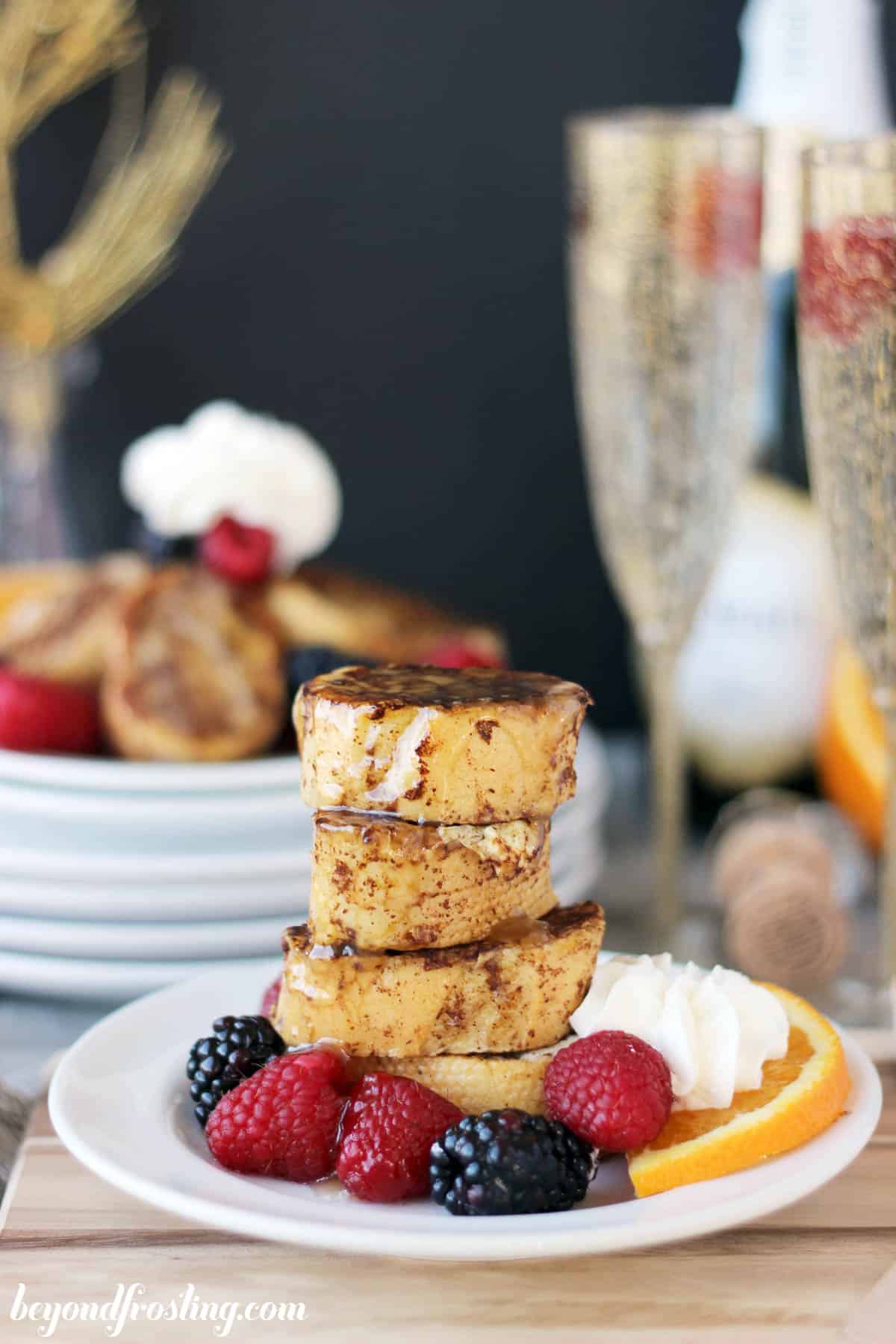 four small pieces of french toast stacked on a plate with berries and an orange slice