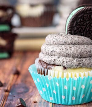 Closeup side view of a cheesecake cupcake topped with frosting and a mint oreo